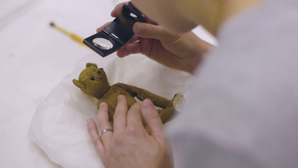 Little Tommy Tittlemouse, being inspected by conservator Nora Meller, with a magnifying glass © Blast! Films – photographer Simon Lloyd 